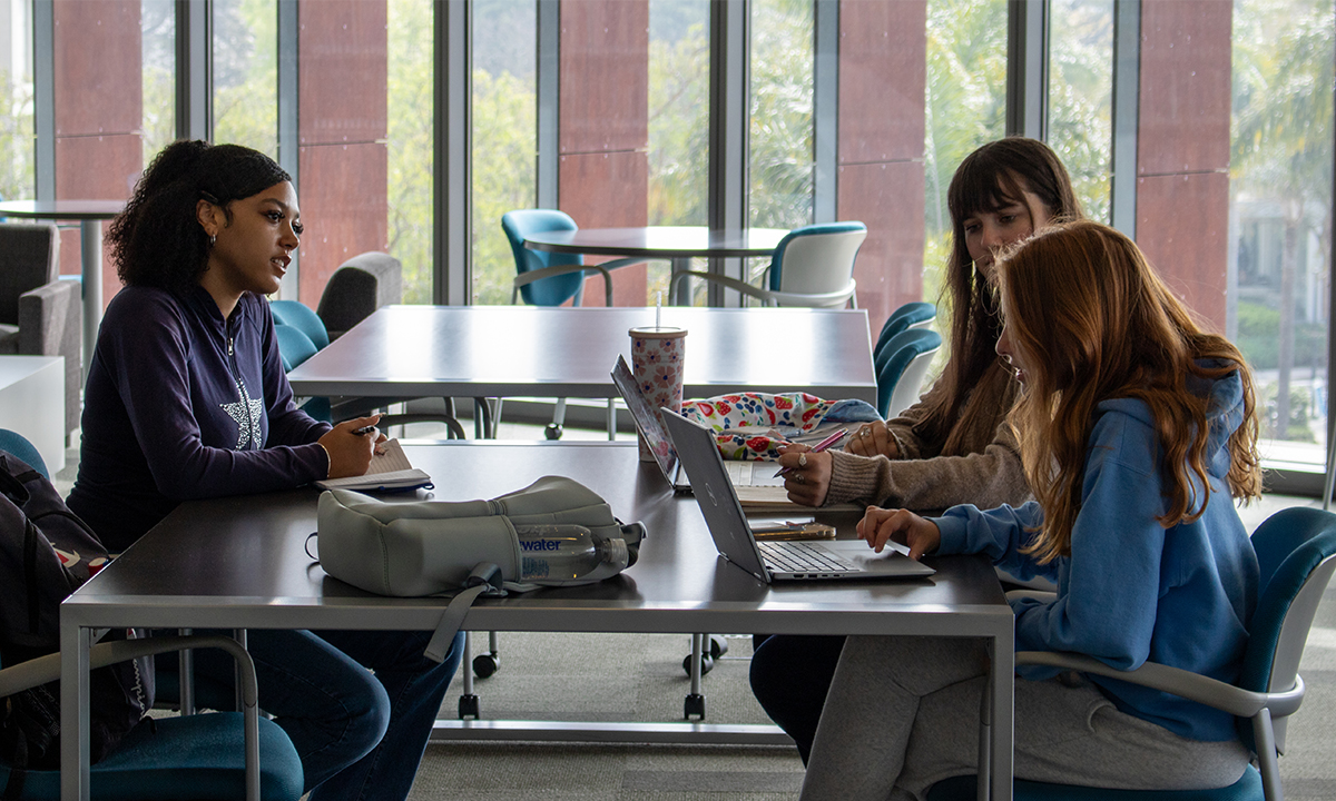 three students at a desk studying